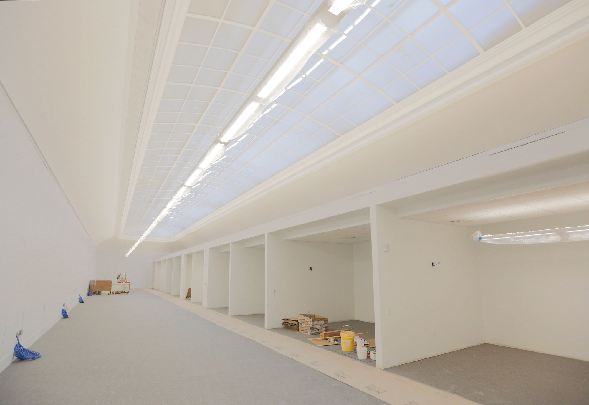 Large white room with glass ceiling with the frame of individual office walls up.