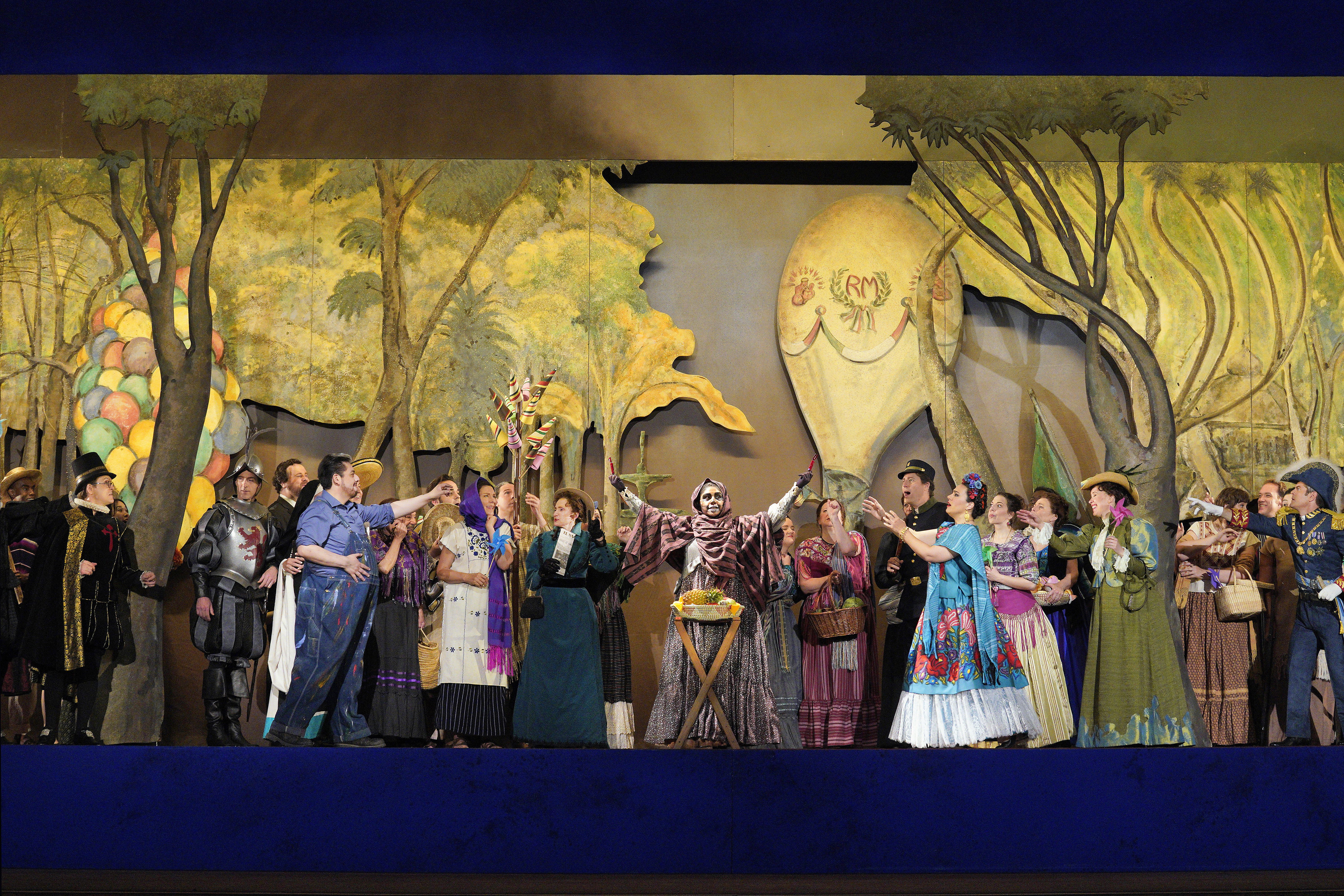 Scene from Frida A group of people standing on stage in front of a painting of forest with a person in skeleton costume at the center