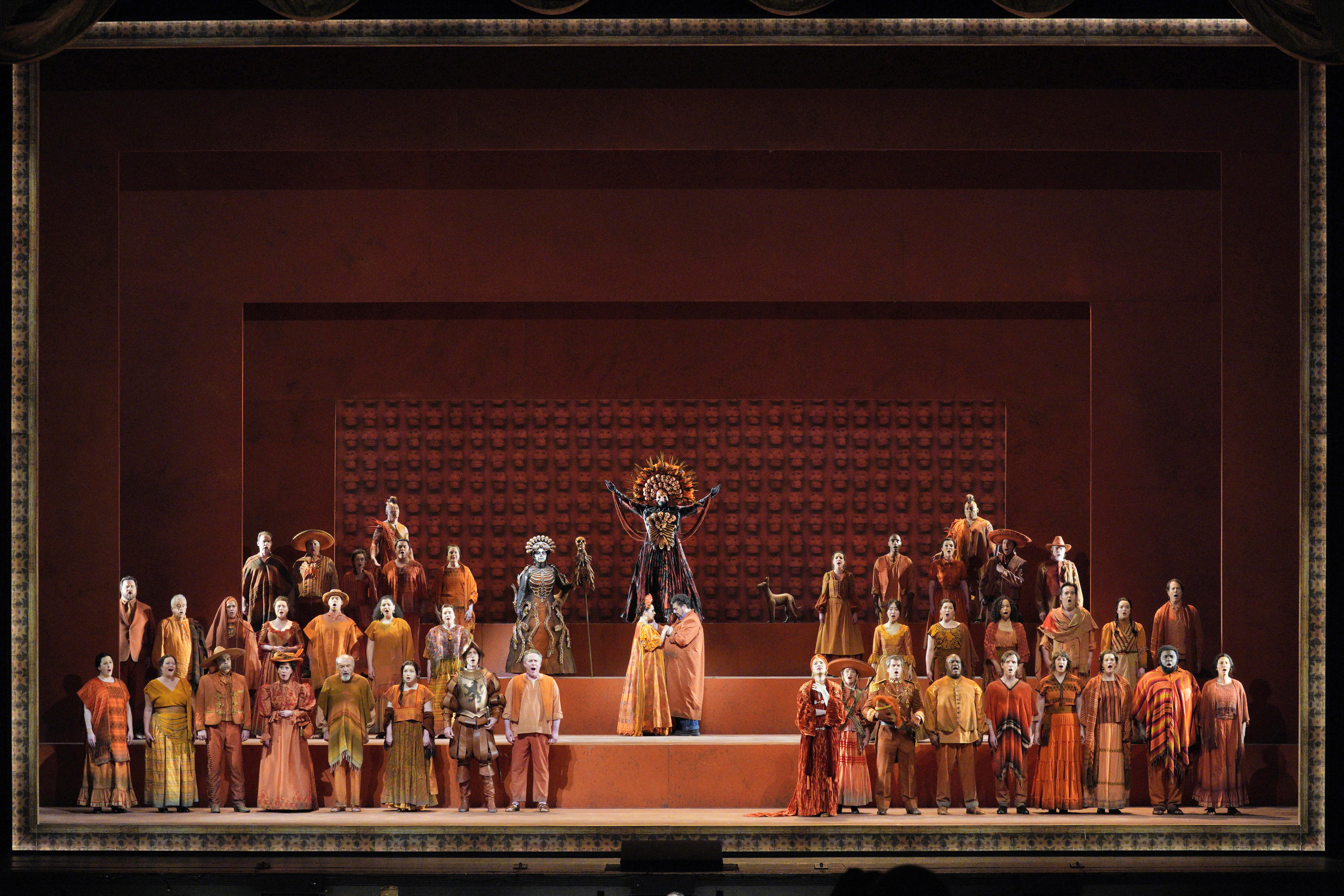 Scene from Frida of a group of people surrounding a man and woman holding hands facing each other while a person dressed in a ceremonial skeleton costume stands behind them with hands raised.