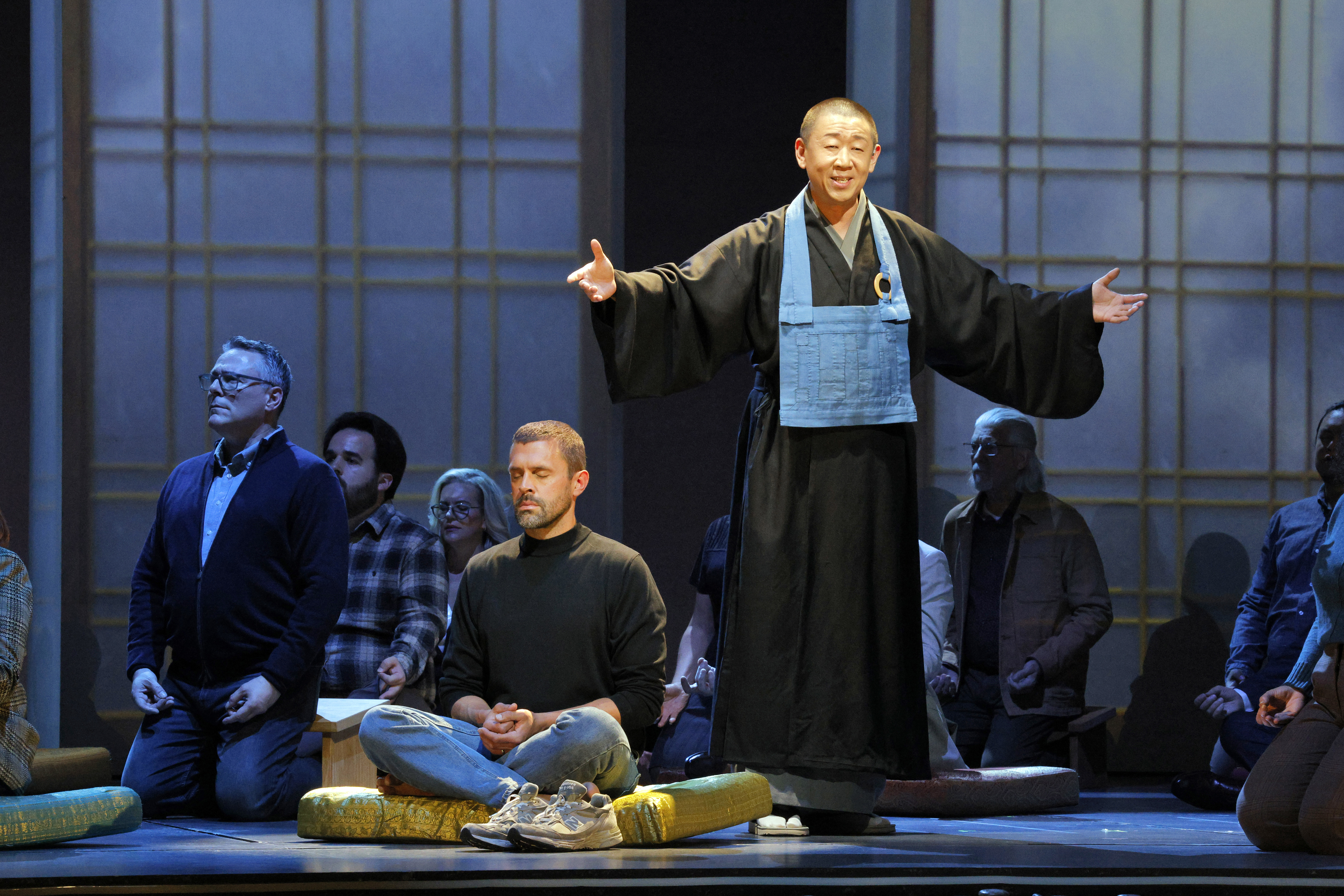 several people sitting cross-legged or kneeling on pads with a guru having his arms outstretched